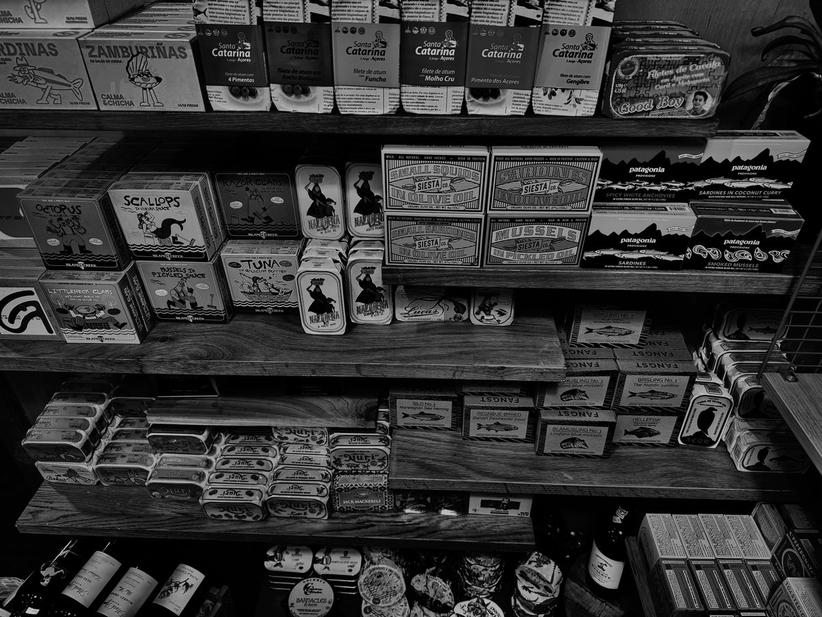 Black-and-white photograph of shelves stocked with tinned fish and conservas at Hinckley's Fancy Meats.